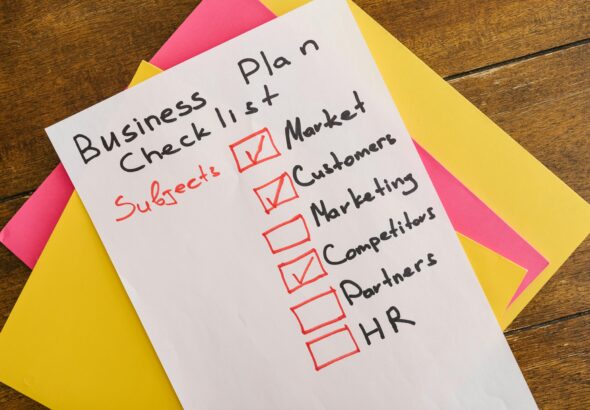 A handwritten business plan checklist on a table with colorful papers indicating important topics for startups.