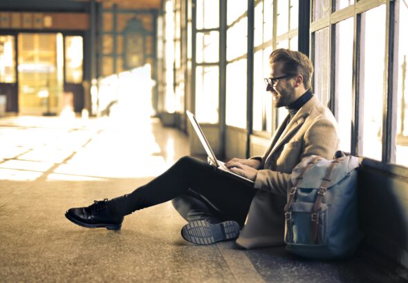 Man sitting by a window at a Budapest train station, working on his laptop with sunlight streaming through.